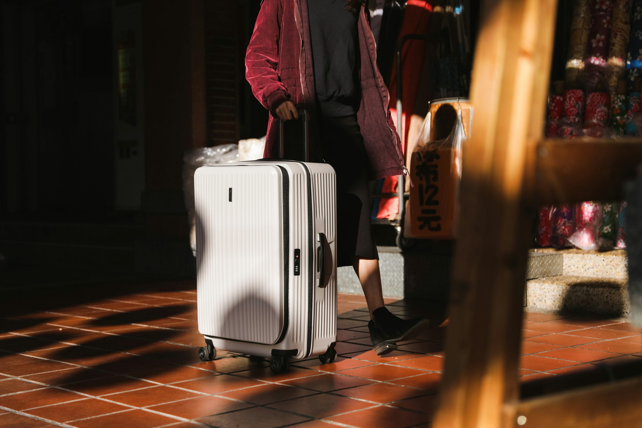 Traveler pulling a white hard-shell suitcase through a warmly lit outdoor market.