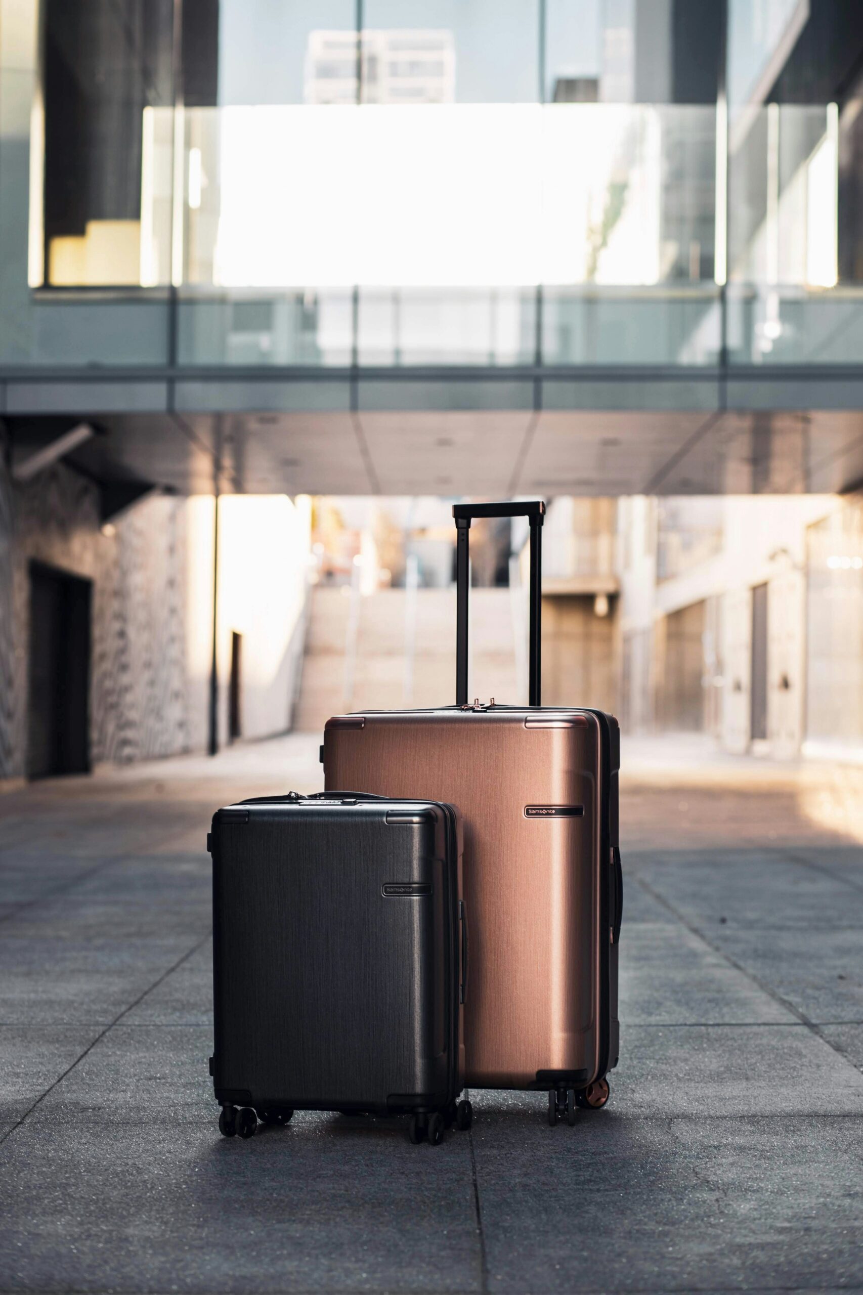 Two modern suitcases standing on a city walkway with a glass building in the background.